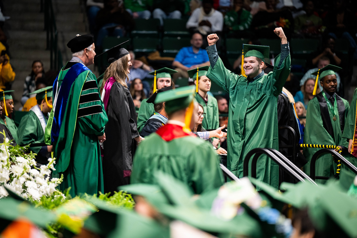 Gay with his hands in the air walking across the stage at commencement