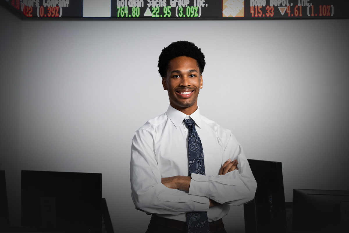 Guy wearing a button up and tie crossing his arms in the middle of a classroom with computers