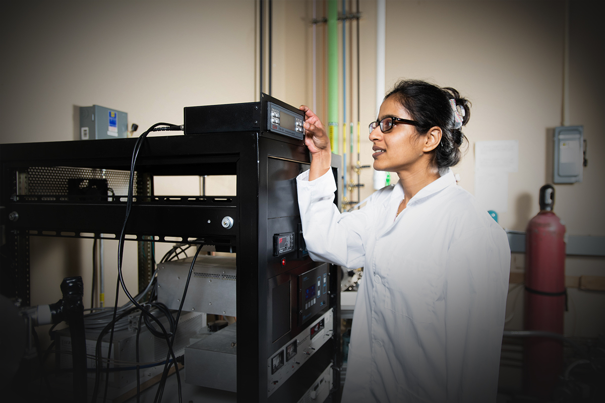 Student in a lab coat hitting buttons on a machine