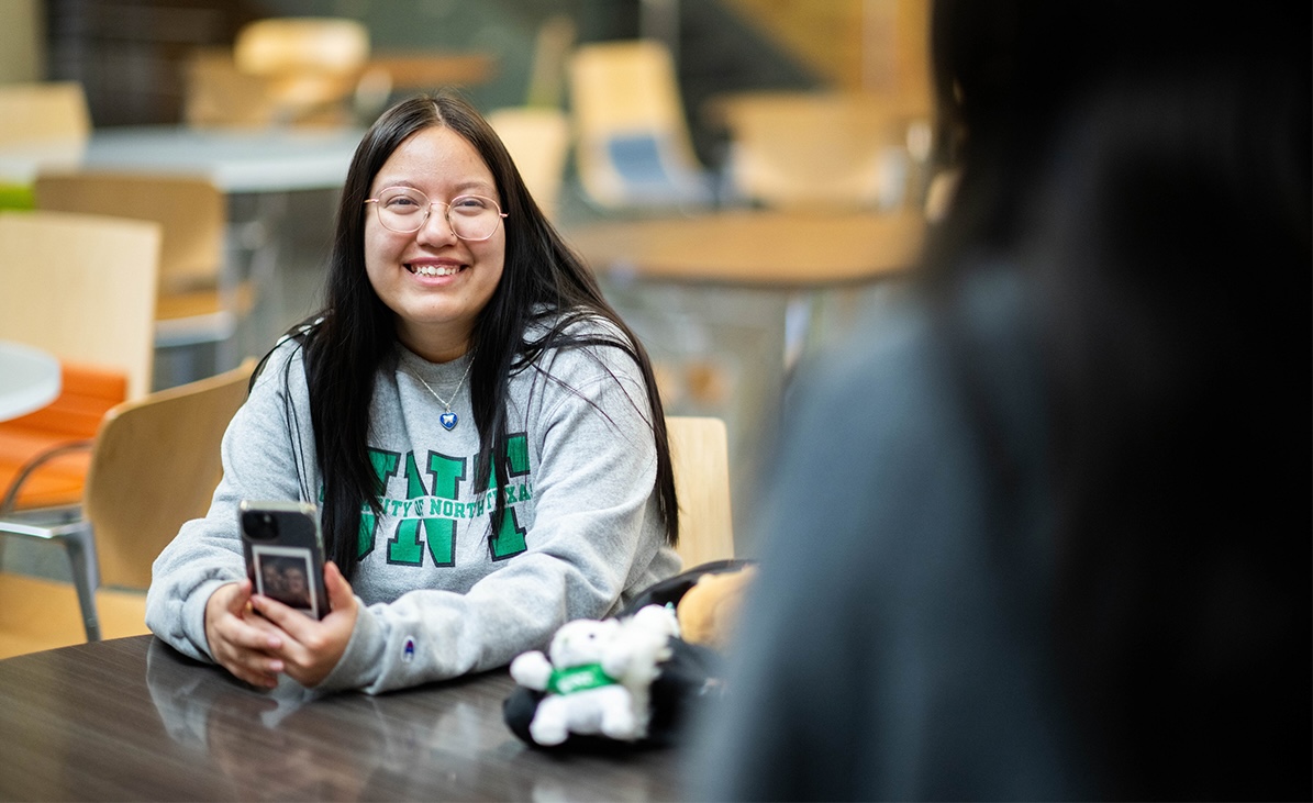 Woman in UNT sweatshirt smiling at a table to another person