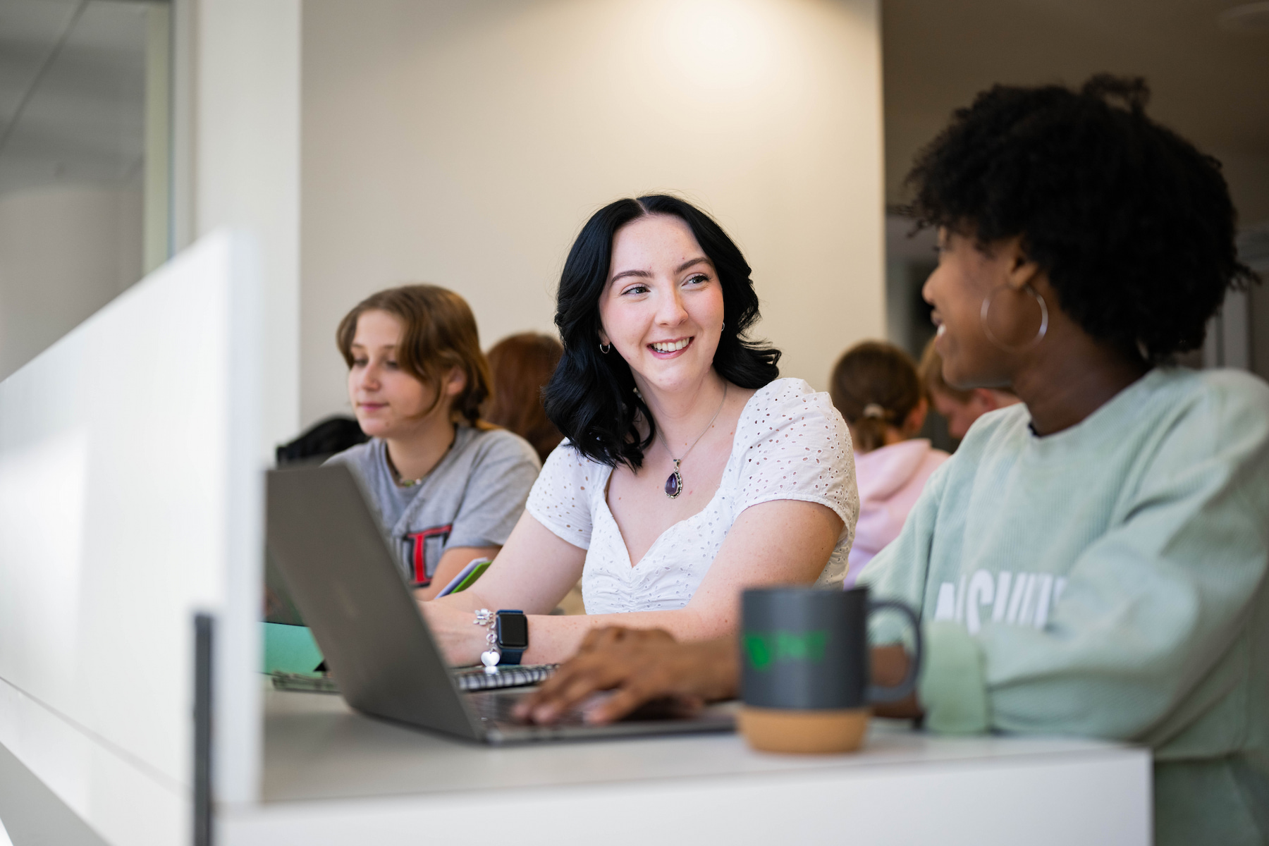 Student speaking with another student at a desk with their laptops out